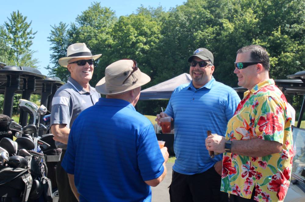 4 men talk by golf carts